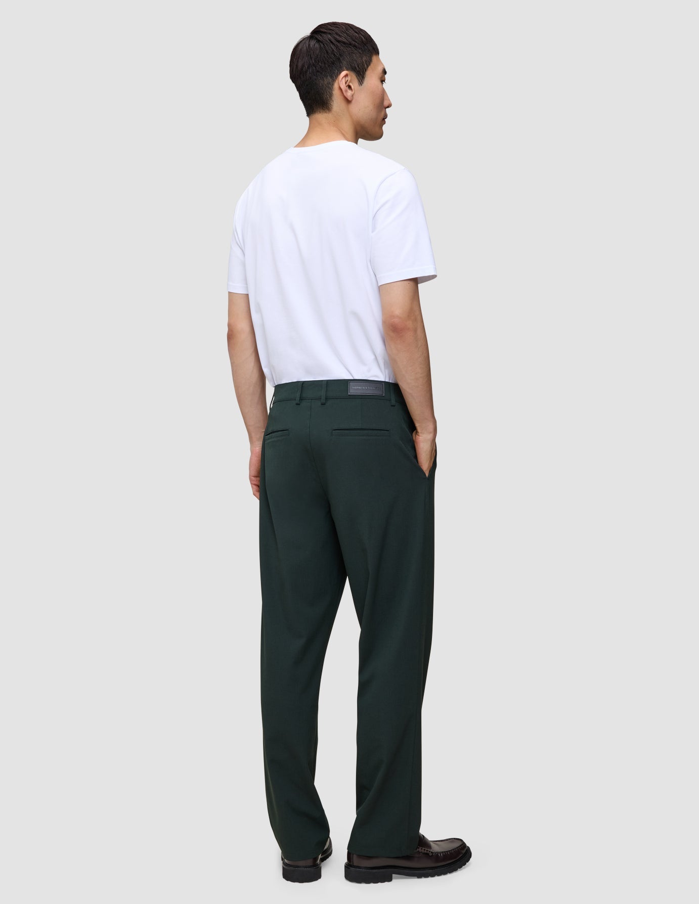 En man sedd bakifrån, klädd i en vit t-shirt och Ease Pants Relaxed Fit Northern Pine i skandinavisk design.